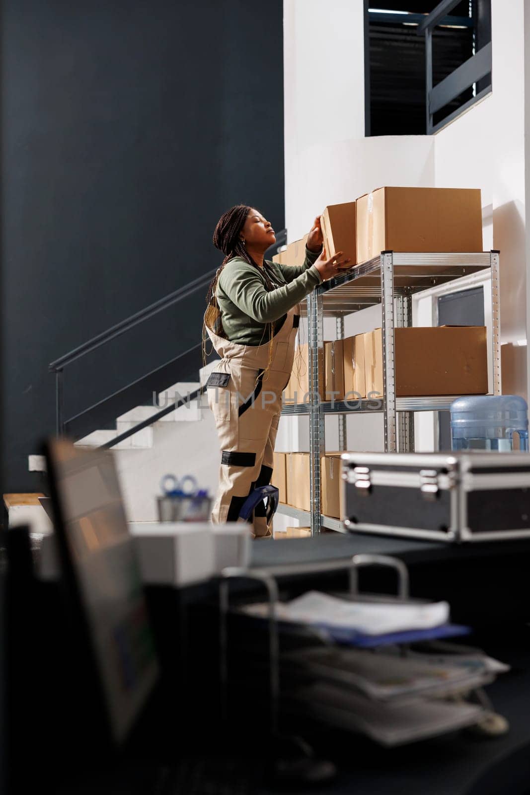 Warehouse employee taking out cardboard box from metallic shelf, working at customers orders in storage room. Stockroom worker preparing packages for delivery during storehouse inventory