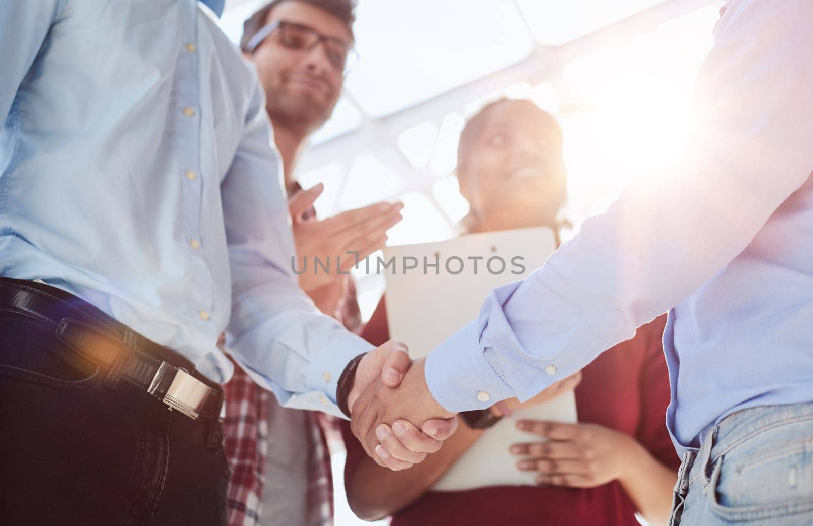 Young startup in casual clothes shaking hands in a modern office space by the window.