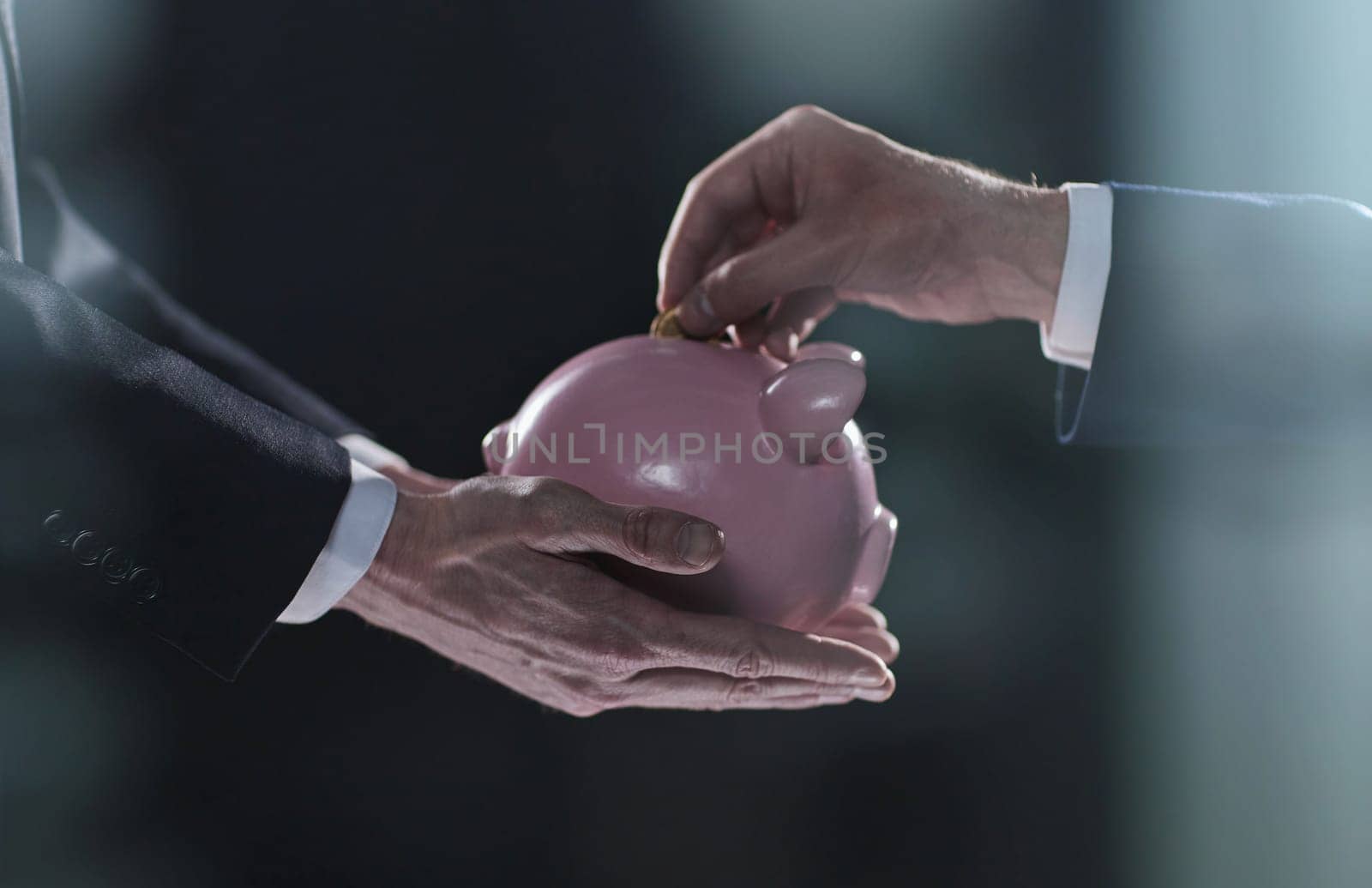 Hand puts a coin in a piggy bank on a black background by Prosto
