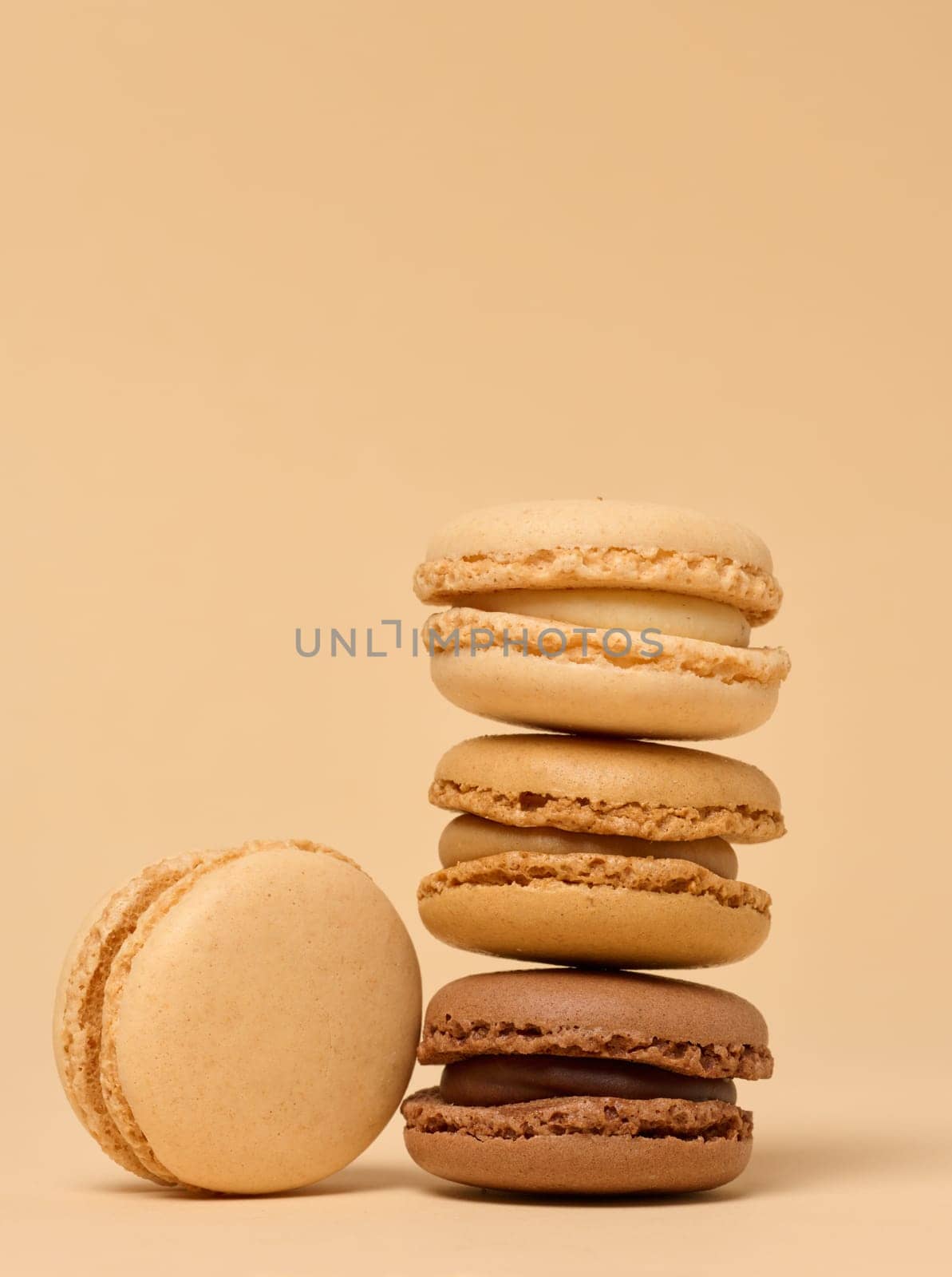 Stack of chocolate macarons on beige background by ndanko