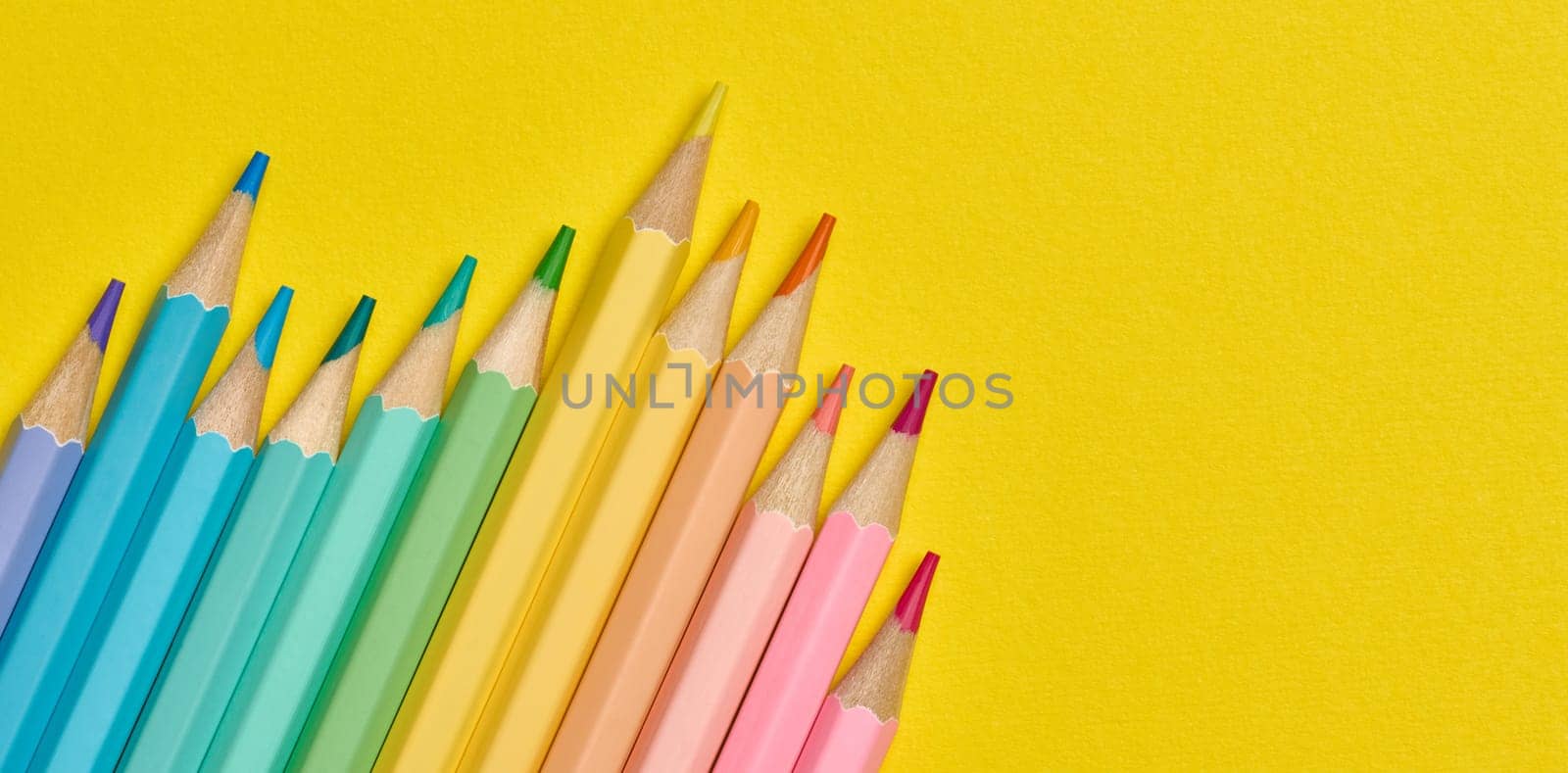 Multi-colored wooden pencils on a yellow background, top view. Copy space