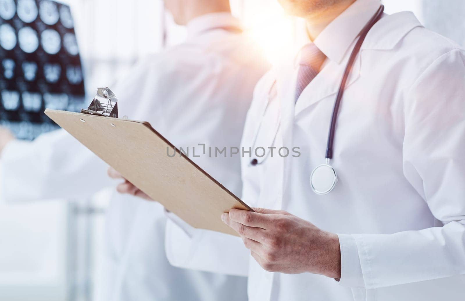 Male doctor on duty in white coat reads patient information by Prosto