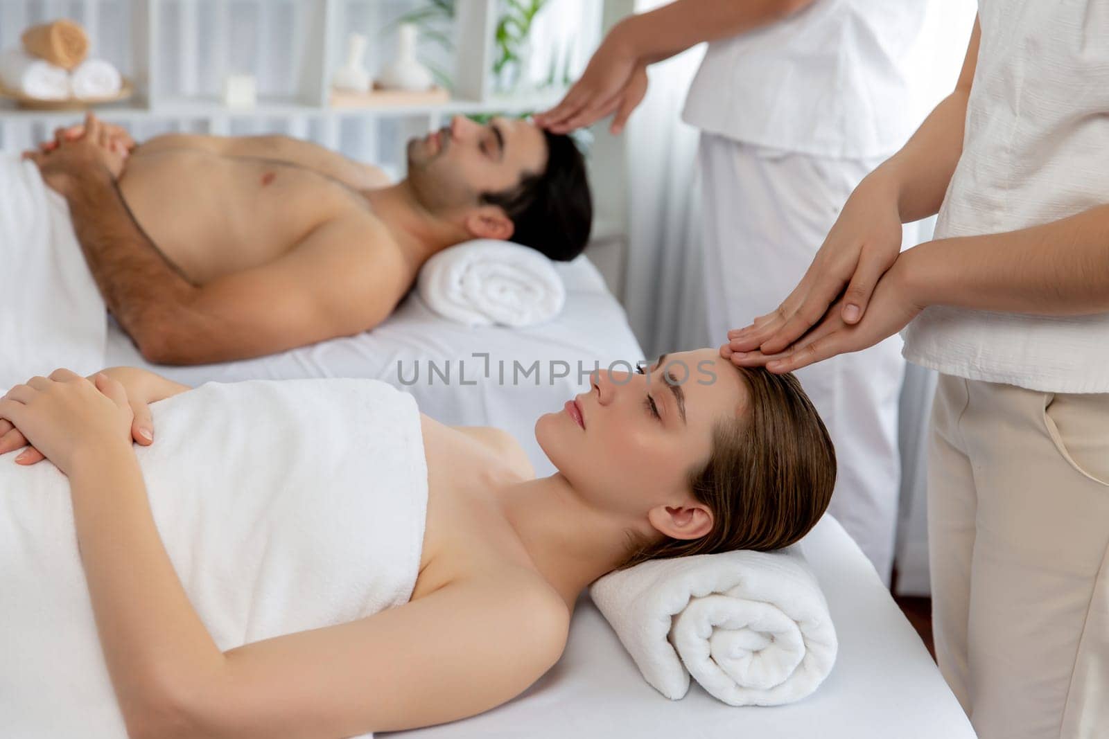 Caucasian couple enjoying relaxing anti-stress head massage and pampering facial beauty skin recreation leisure in dayspa modern light ambient at luxury resort or hotel spa salon. Quiescent