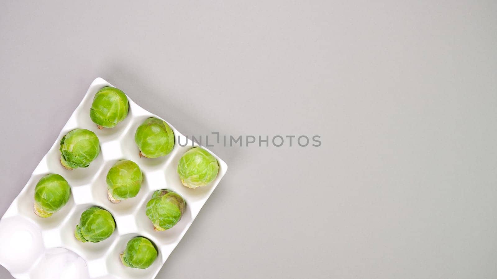 Raw organic Brussel sprouts in yellow white egg container on grey background, top view. Flat lay, overhead, from above. Copy space.