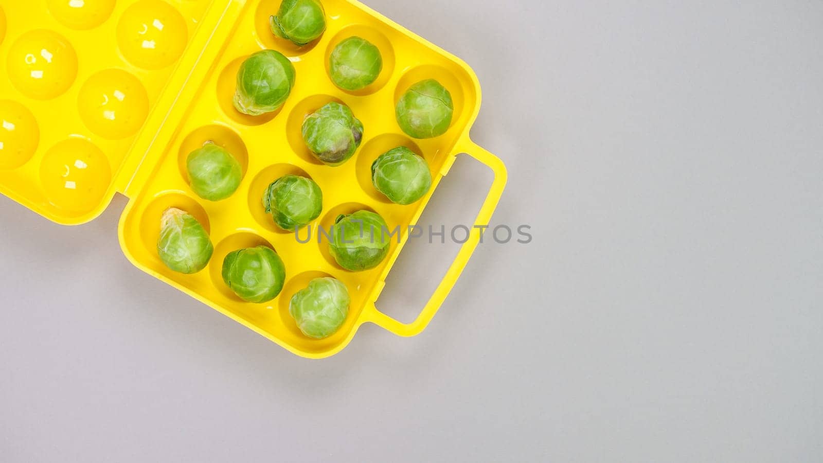 Raw organic Brussel sprouts in yellow container on grey background, top view. Flat lay, overhead, from above. Copy space