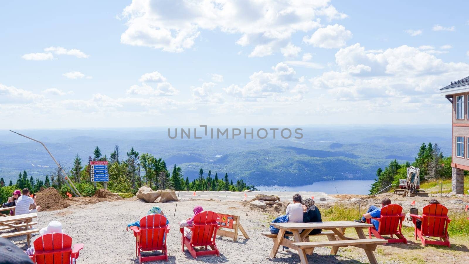 Sightseeing mountain views at Mont Tremblant ski Resort in summer. Tourists enjoying sitting at red chairs at ski resort village. Mont-Tremblant, Quebec, Canada - 22.09.2022.