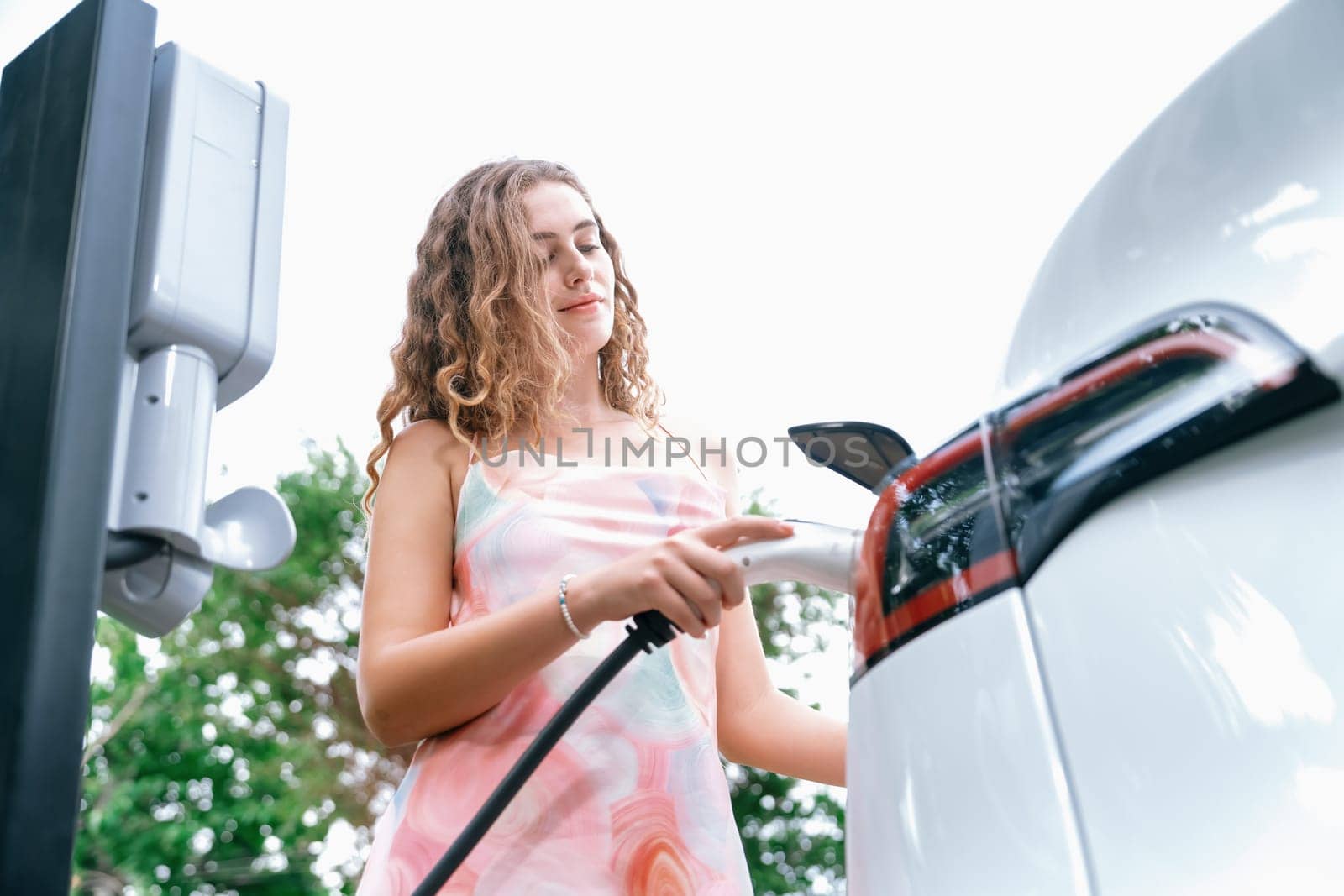 Eco-friendly conscious woman recharging modern electric vehicle. Synchronos by biancoblue