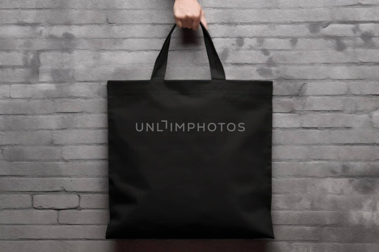 Hand holding black cotton tote bag mockup on a wall background.