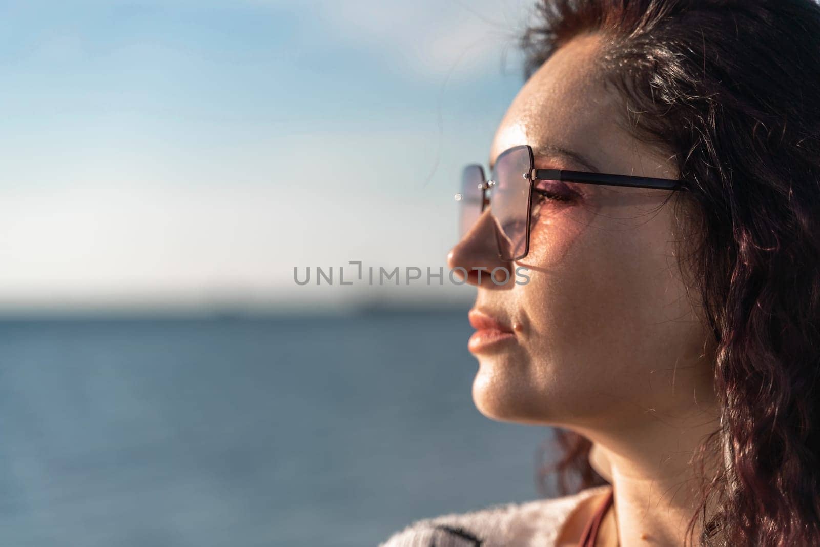 Portrait of a curly woman in glasses on the background of the sea. Vacation on the sea, walk, tourism. by Matiunina