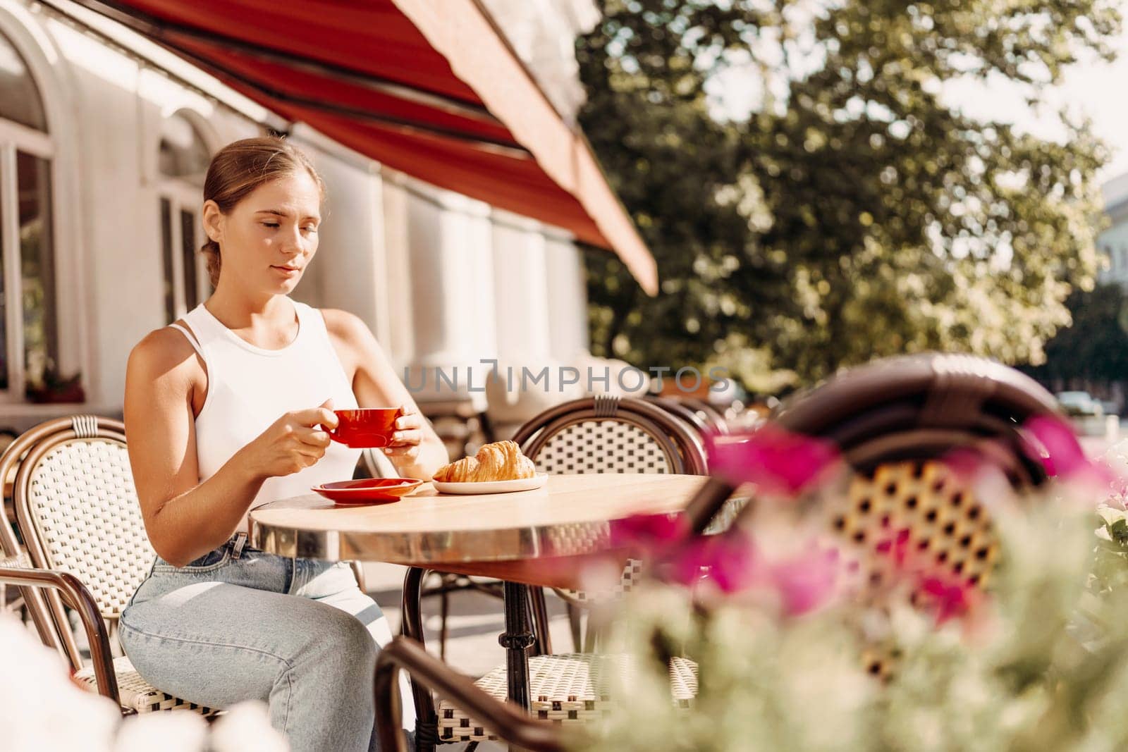 Portrait of happy woman sitting in a cafe outdoor drinking coffee. Woman while relaxing in cafe at table on street, dressed in a white T-shirt and jeans.