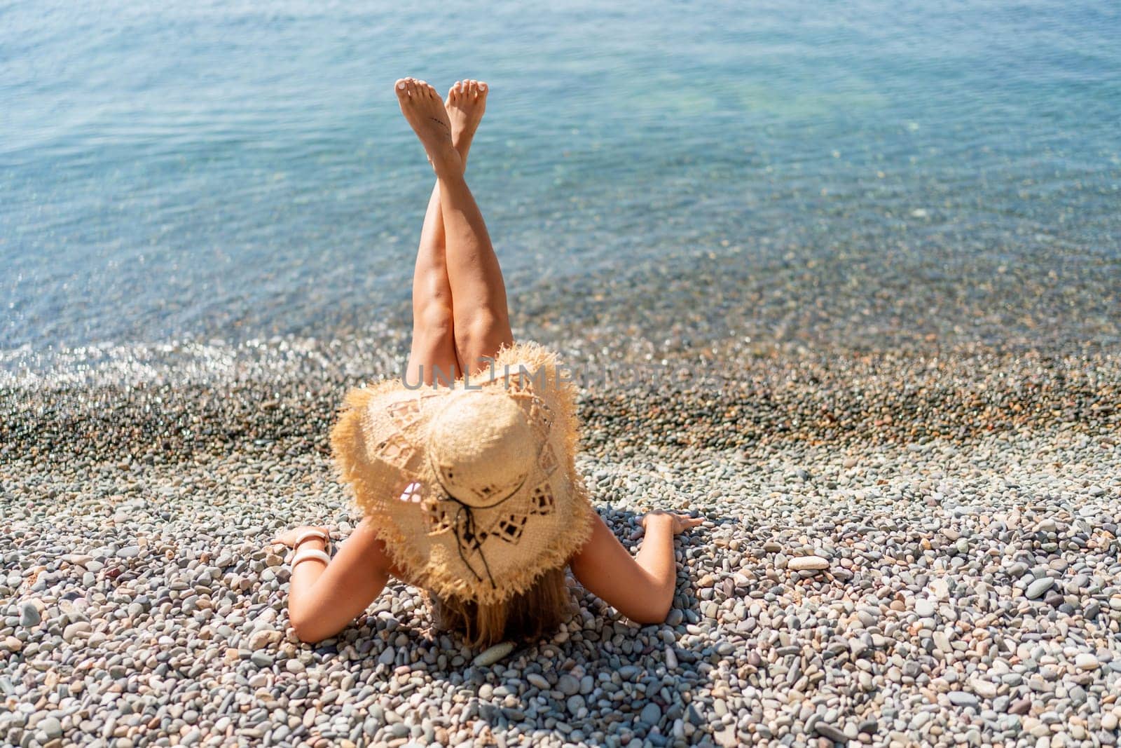 Beach Relaxation woman lies on a pebble beach, legs raised, and arms spread out. The concept of travel, vacation at sea.