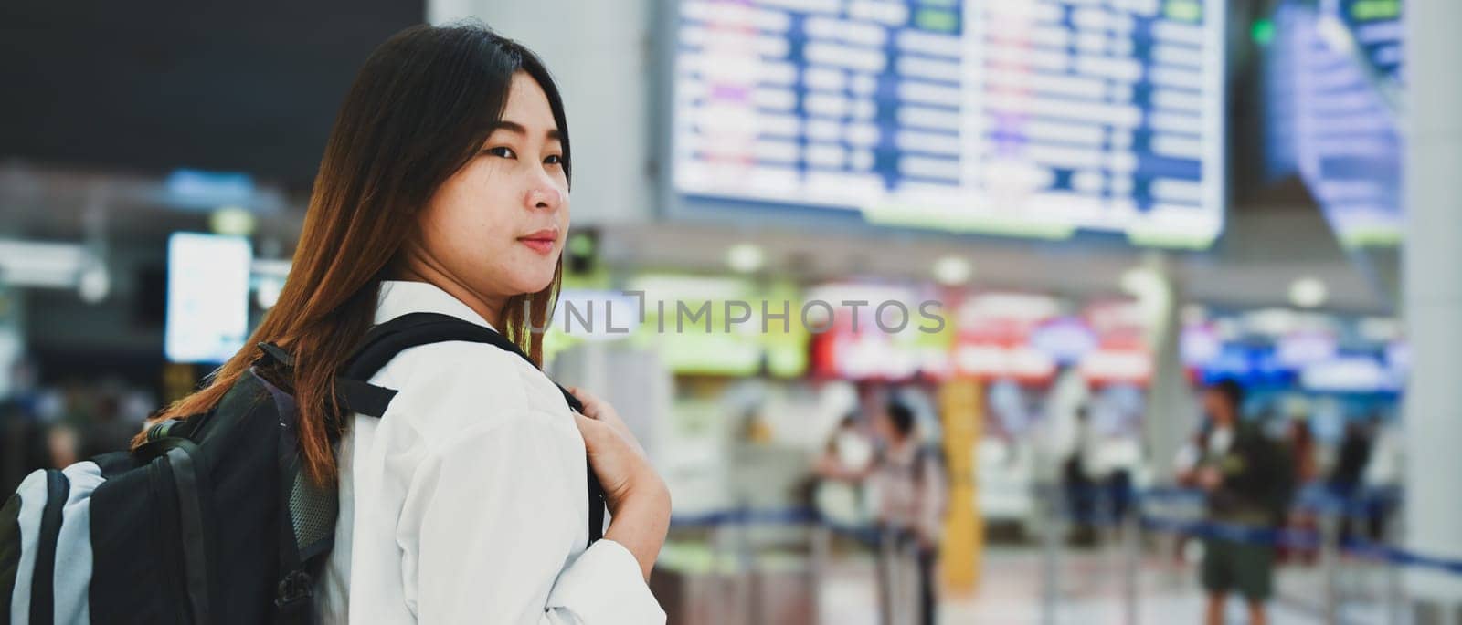 Happy young woman with backpack waiting for boarding at airport by prathanchorruangsak