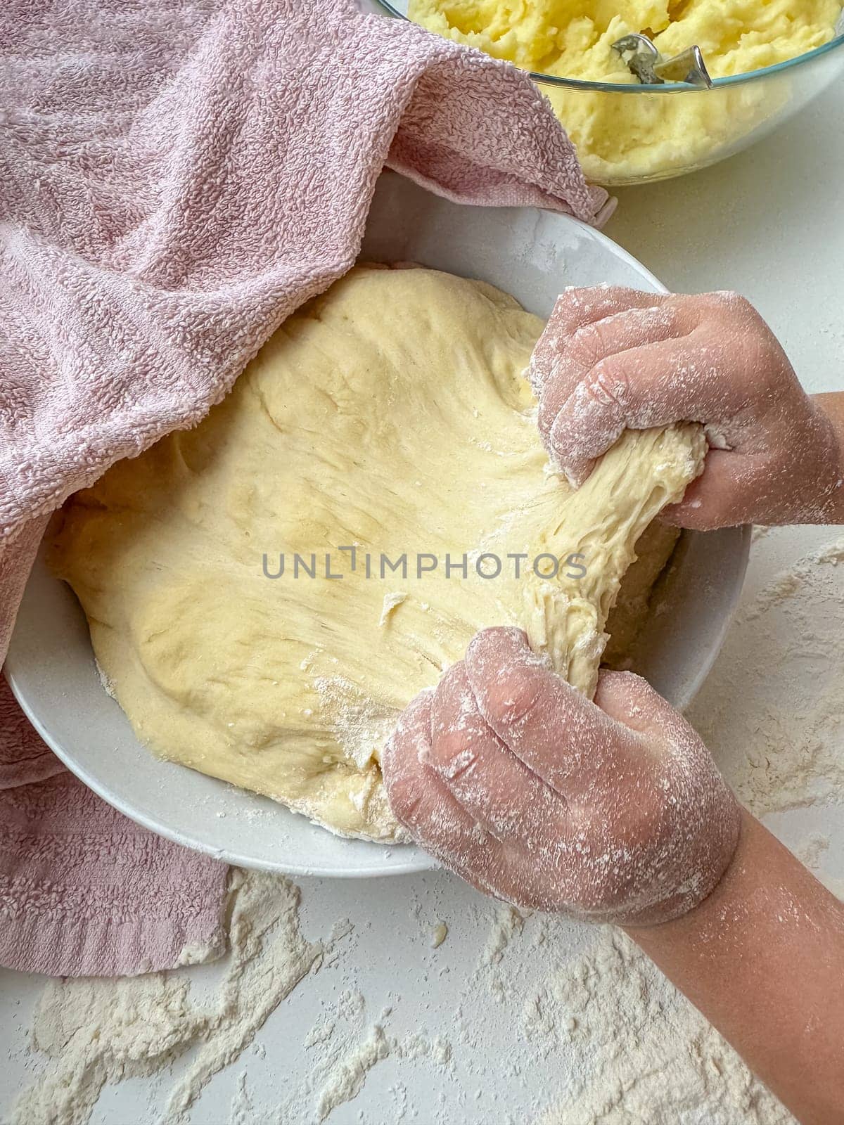 The hands of child knead the dough for making pies on white table, top view. High quality photo