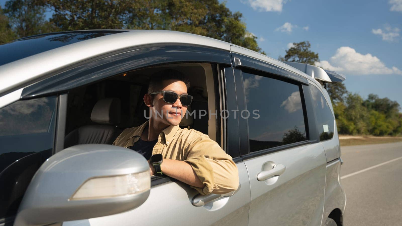 Happy solo traveler leaning out of car window enjoying freedom during road trip. Travel and active lifestyle concept.