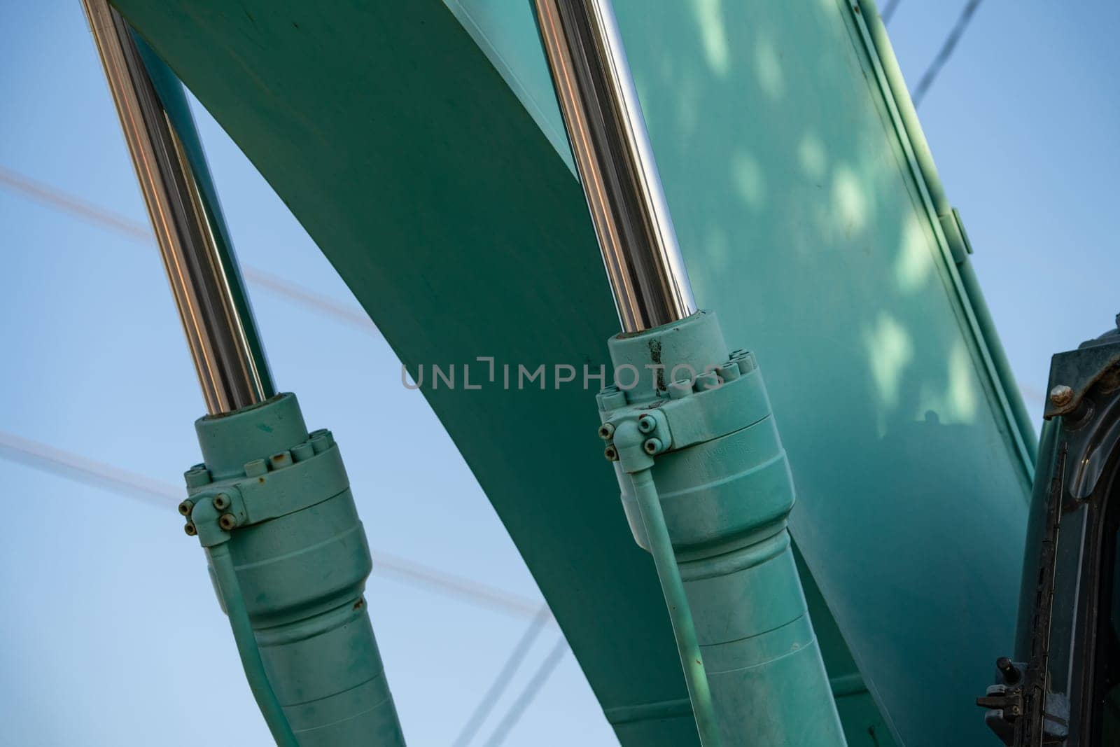Closeup view of stainless steel hydraulic arm on green excavator. Stainless steel power in the hydraulic arm of an excavator. Stainless steel hydraulic arm of excavator unveils industrial precision.
