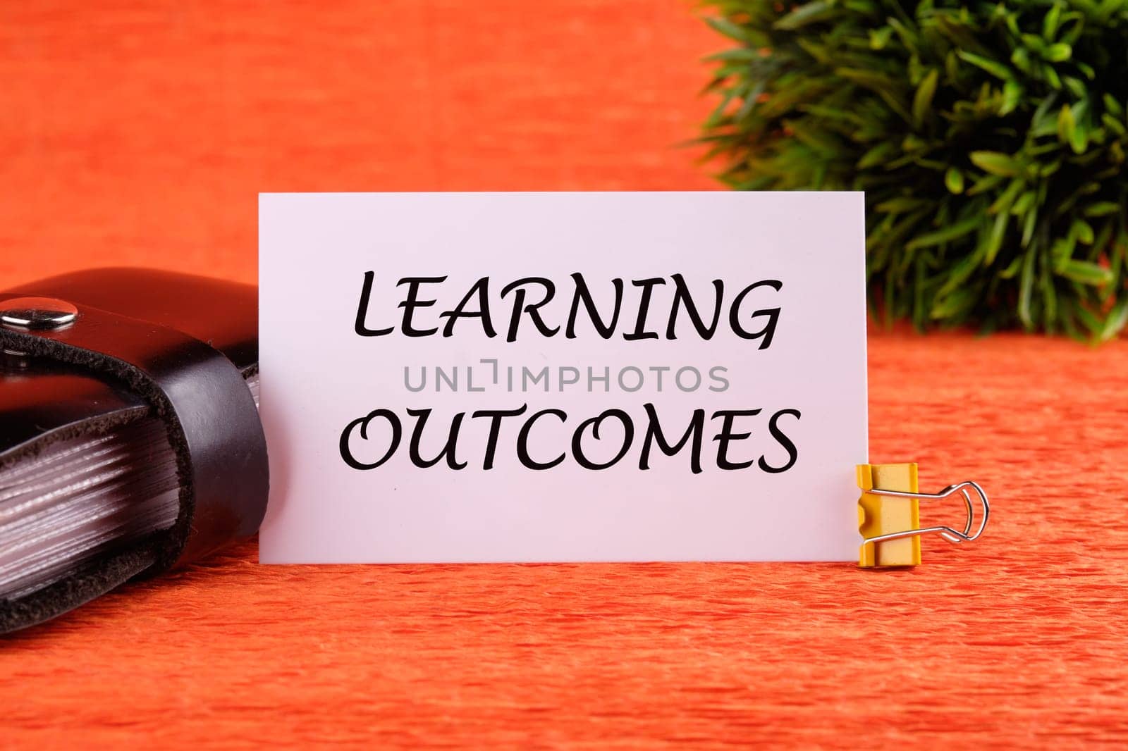 Learning Outcome write on a white card near the business card holder in black on an orange background