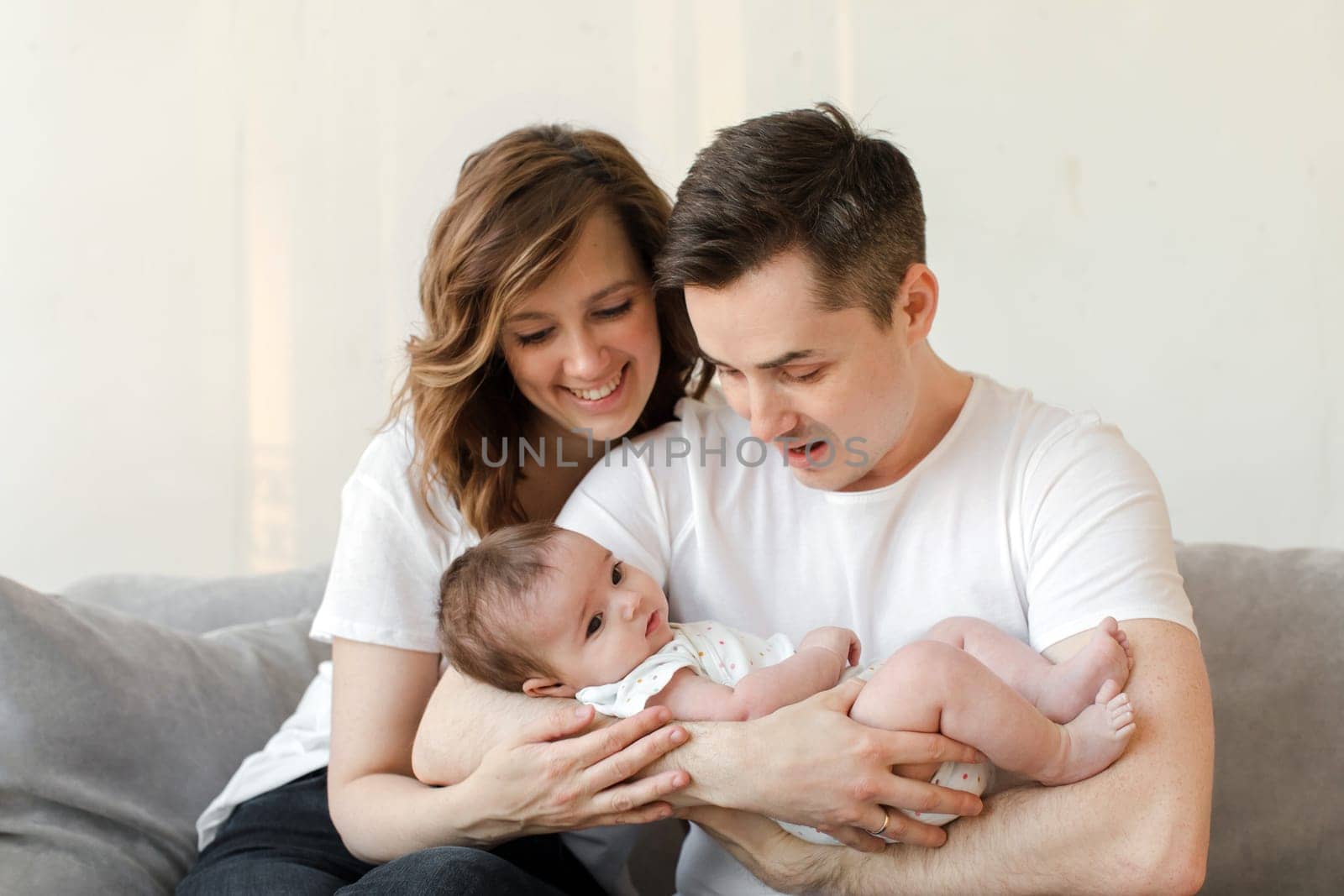 Cheerful couple sitting on sofa and carrying cute baby by Demkat