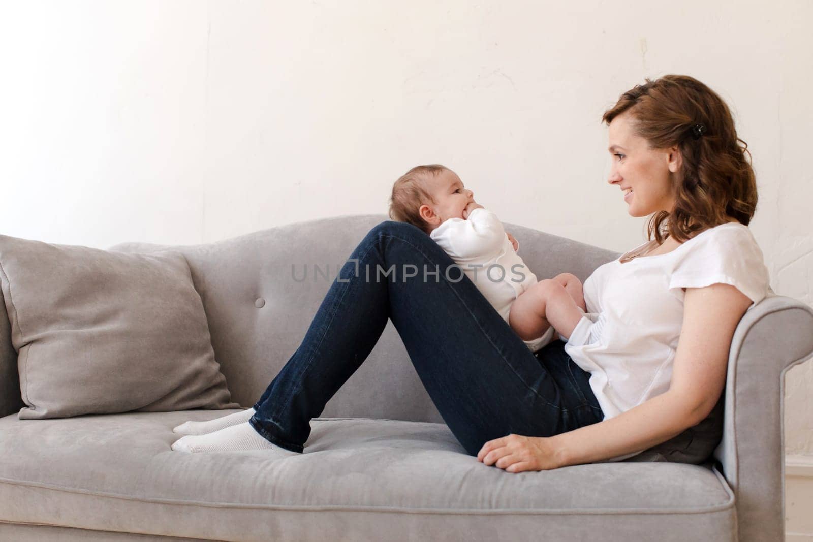 Happy mother with baby sitting on sofa by Demkat