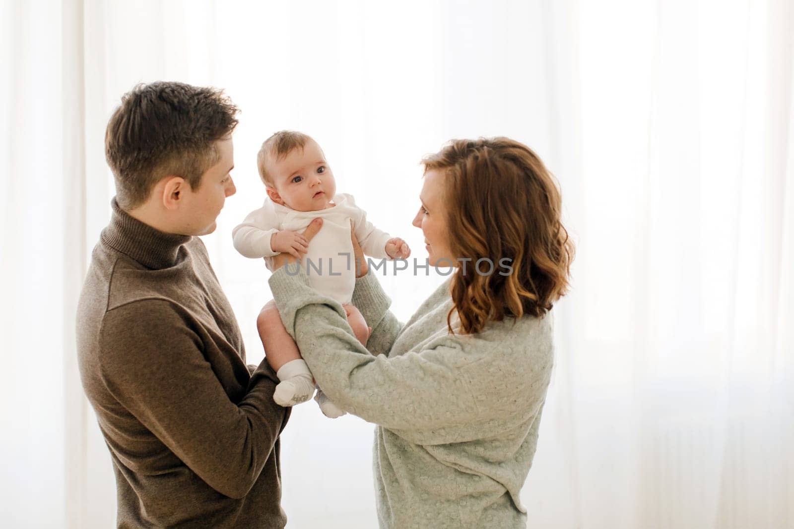 Happy couple carrying adorable baby near curtain by Demkat