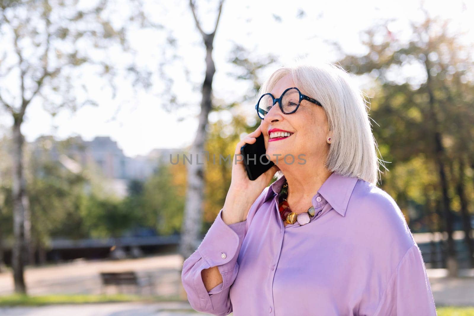senior woman smiling happy talking by mobile phone while walking outdoors, concept of technology and elderly people leisure, copy space for text