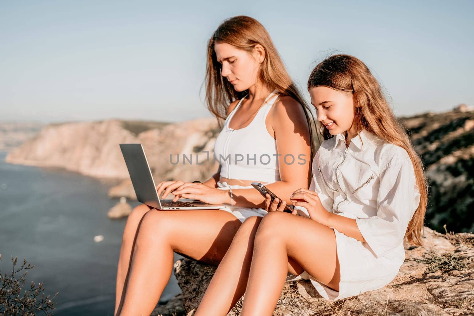 Successful business woman in yellow hat working on laptop by the sea. Pretty lady typing on computer at summer day outdoors. Freelance, travel and holidays concept.