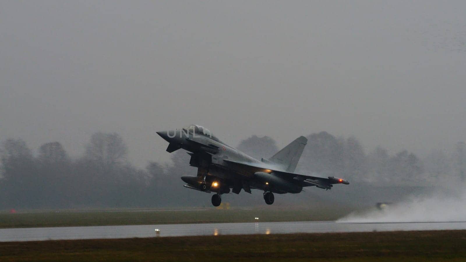 Istrana Italy December 13 2023: Combat aircraft lifts off a flooded runway, casting massive water clouds. Includes copy space. NATO air defense capability in all weather. Copy Space.