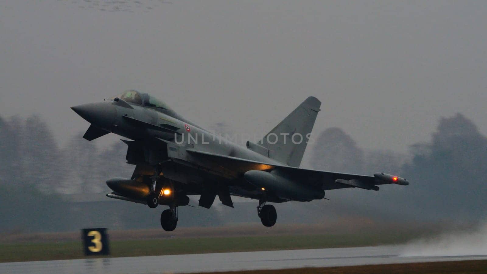 Istrana Italy December 13 2023: Combat aircraft lifts off a flooded runway, casting massive water clouds. Includes copy space. NATO air defense capability in all weather. Copy Space.