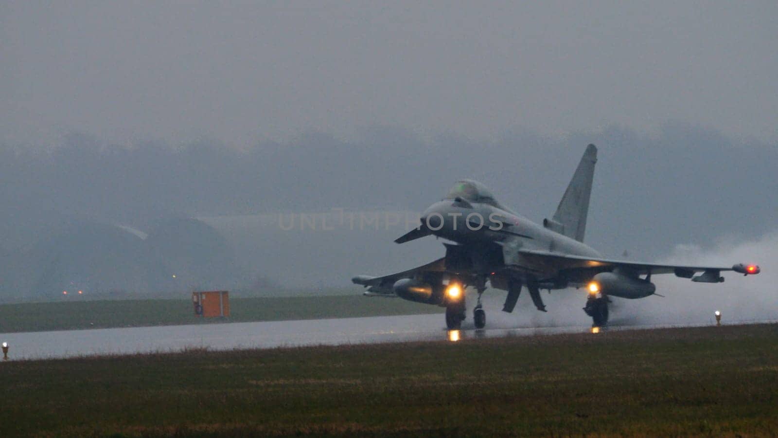 Istrana Italy December 13 2023: Combat aircraft lifts off a flooded runway, casting massive water clouds. Includes copy space. NATO air defense capability in all weather. Copy Space.