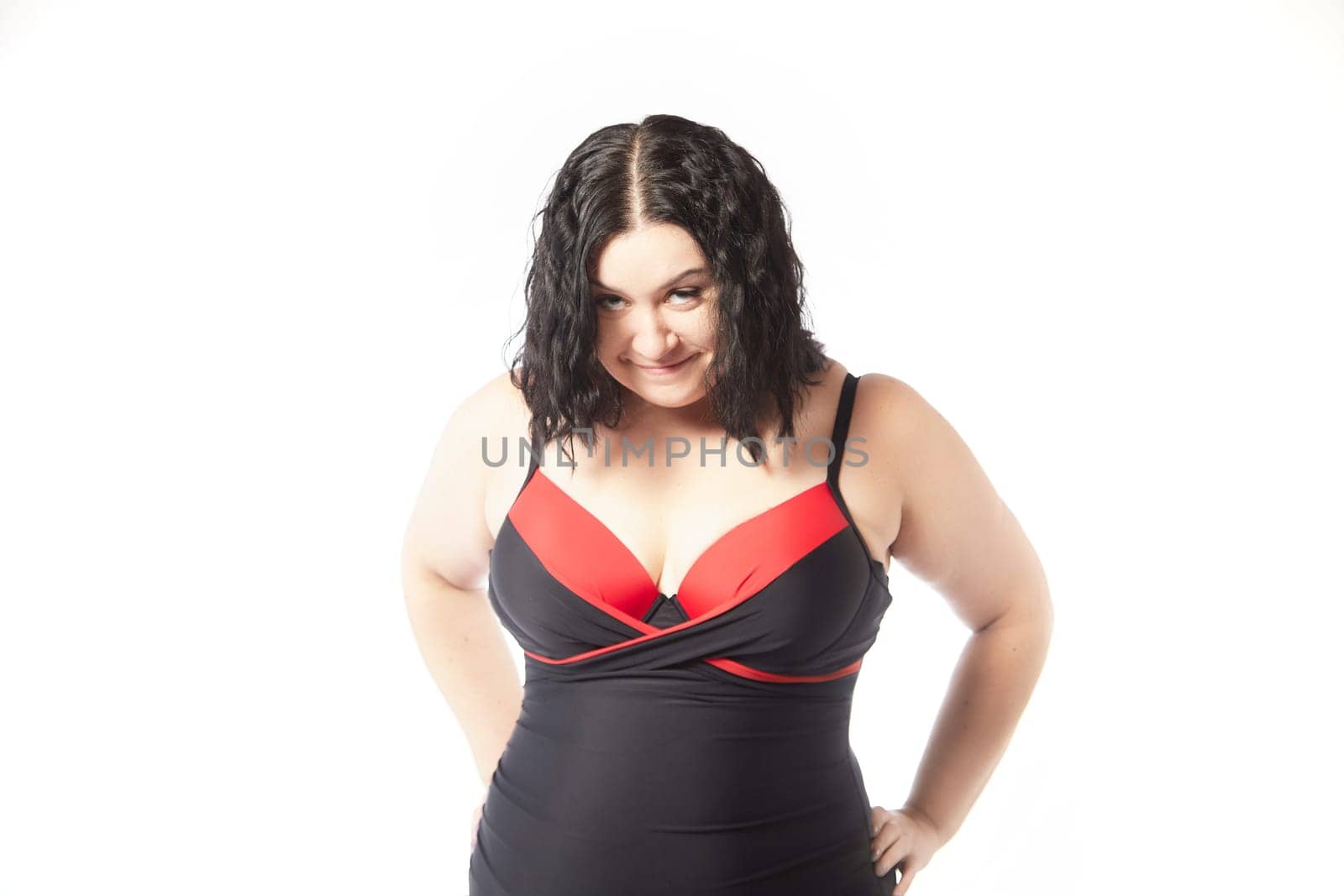 Portrait of attractive dreamy thick woman in red black swimsuit posing on white background. Body positive, photoshoot, selfie. Funny plus size model