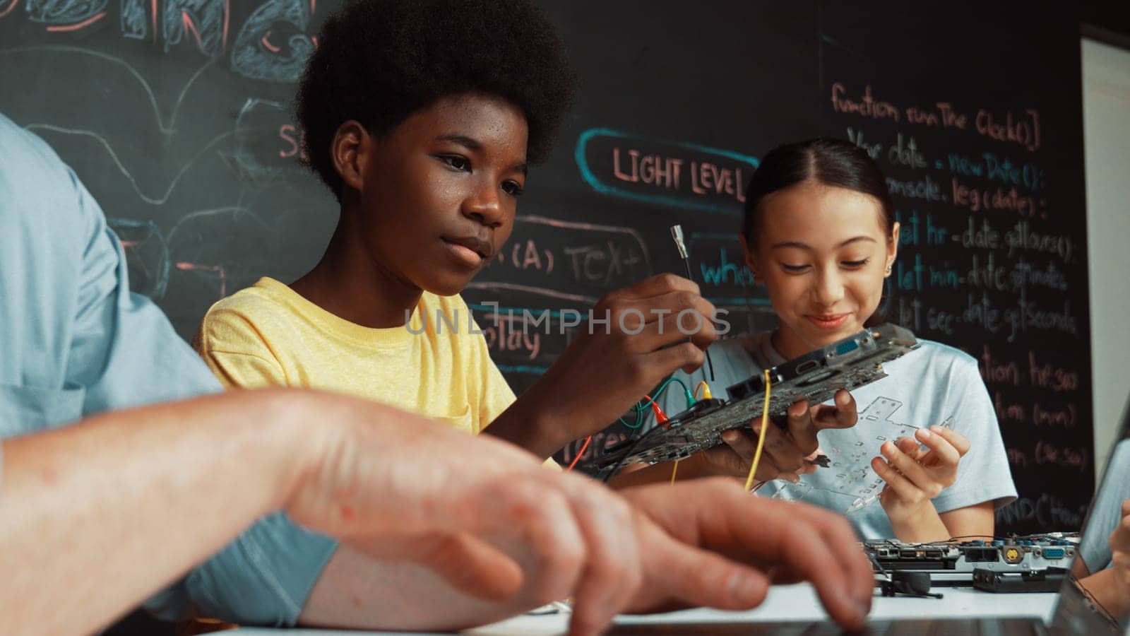 Young student fixing controller while teacher programing engineering code at STEM class. Closeup of instructor hand typing computer while smart girl using electronic tool and blackboard. Edification.