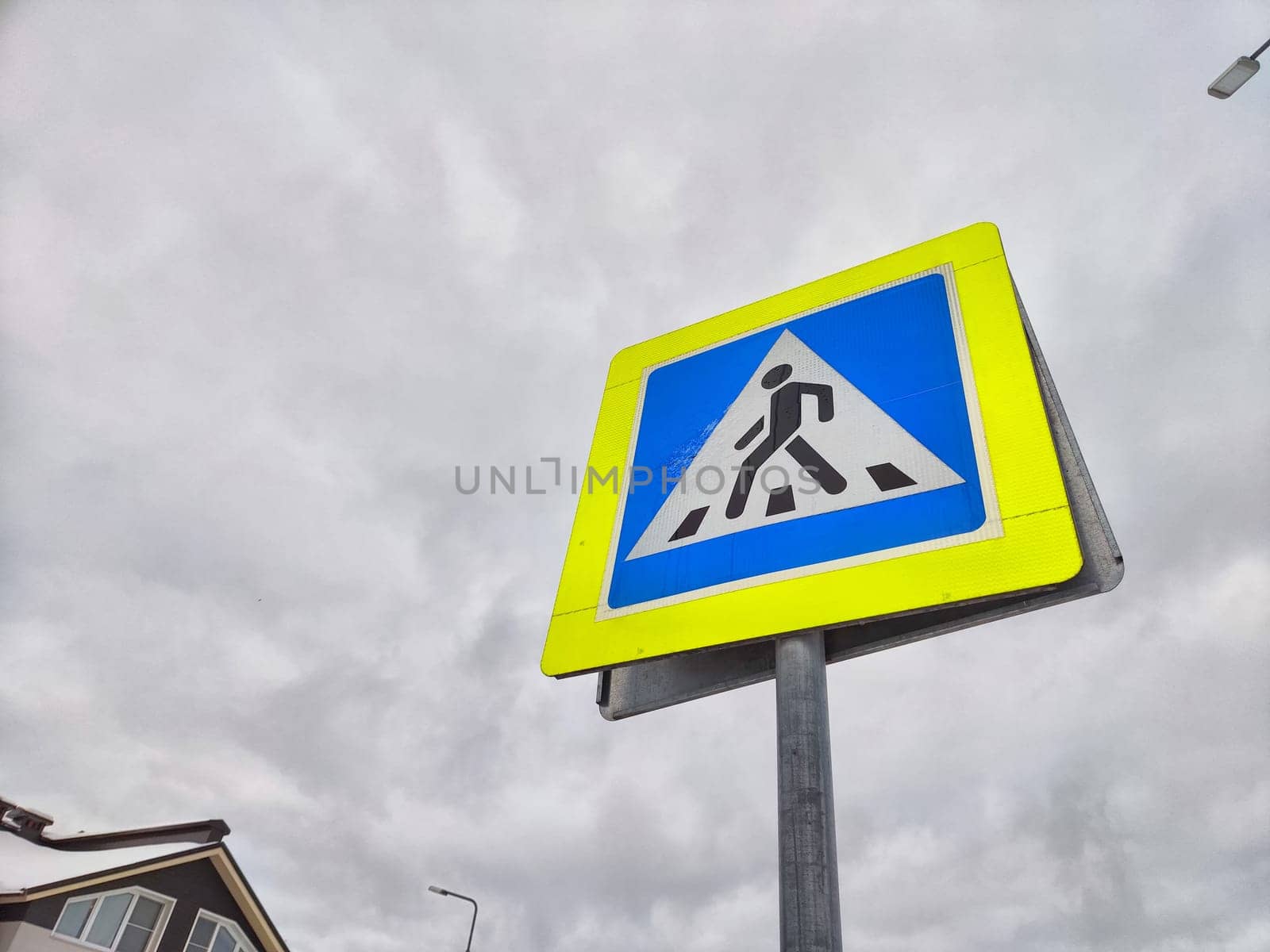A pedestrian crossing sign on the background of a gray sky with clouds. Drawing, pictogram for pedestrians crossing the road