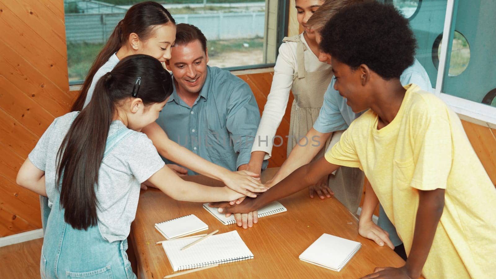 Caucasian teacher and diverse children putting hand together to celebrate successful project or encourage in classroom. Represent love, corporate, team working, togetherness and unity. Edification.