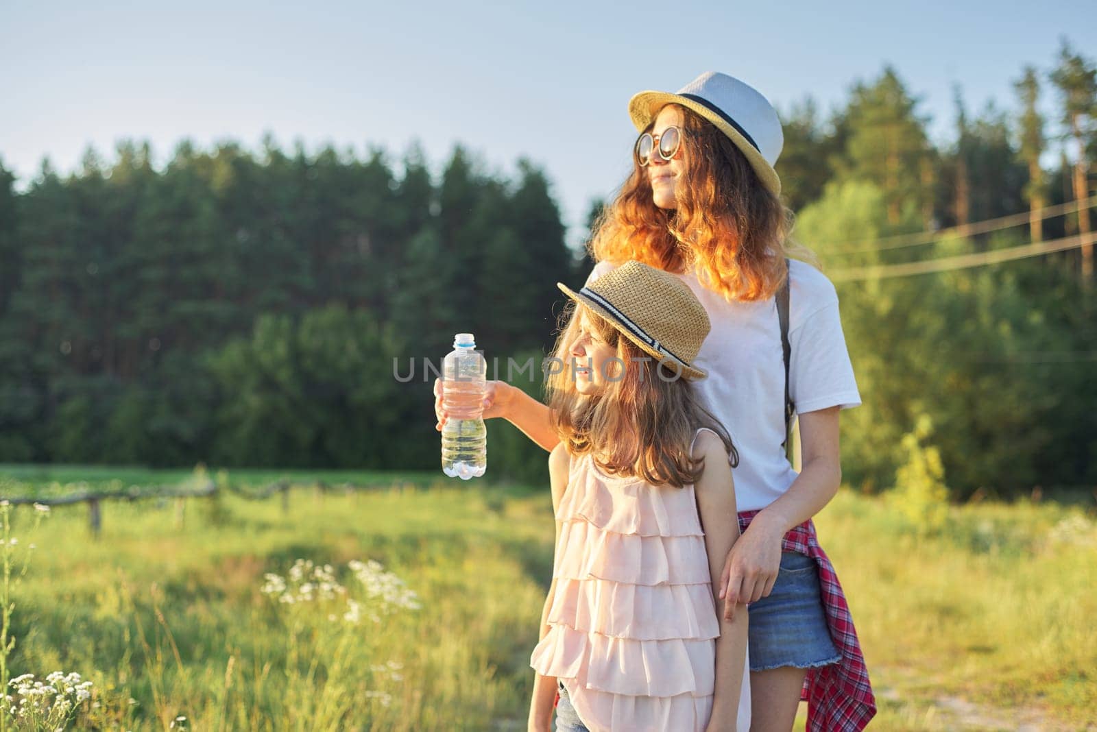 Children two girls sisters with bottle of water on hot summer day in nature, rural landscape, country road background