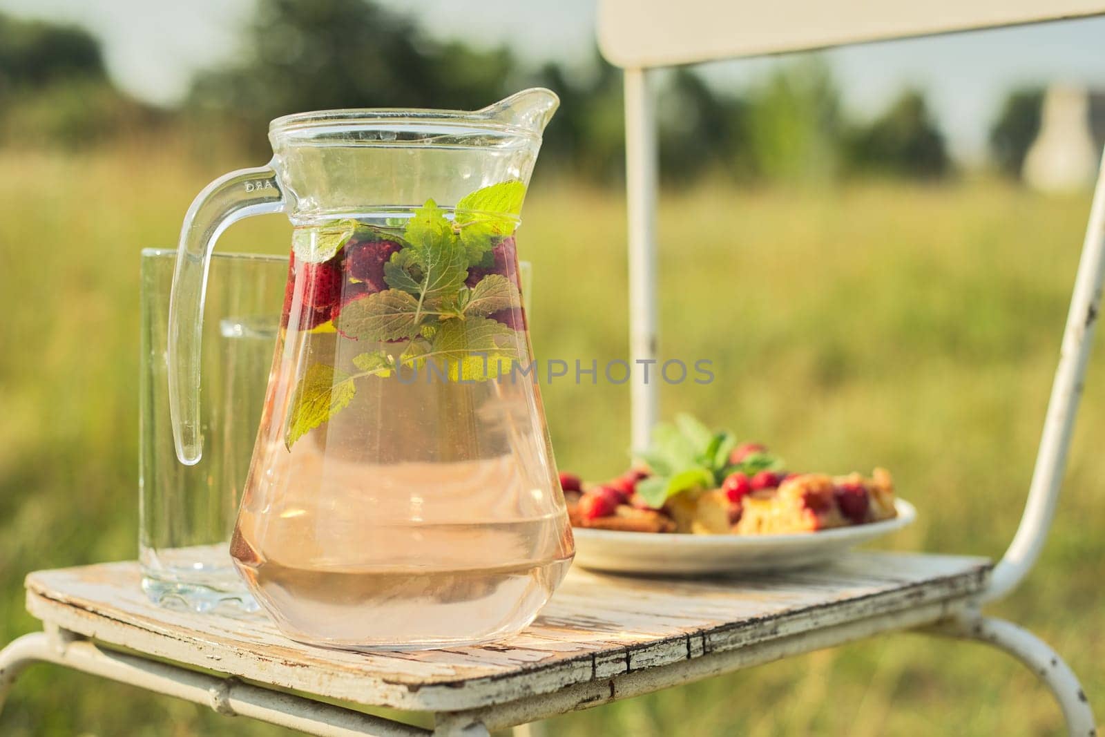 Hello summer, strawberry season. Cake with berries and jug with strawberry mint drink on vintage chair in summer sunny meadow, background nature grass