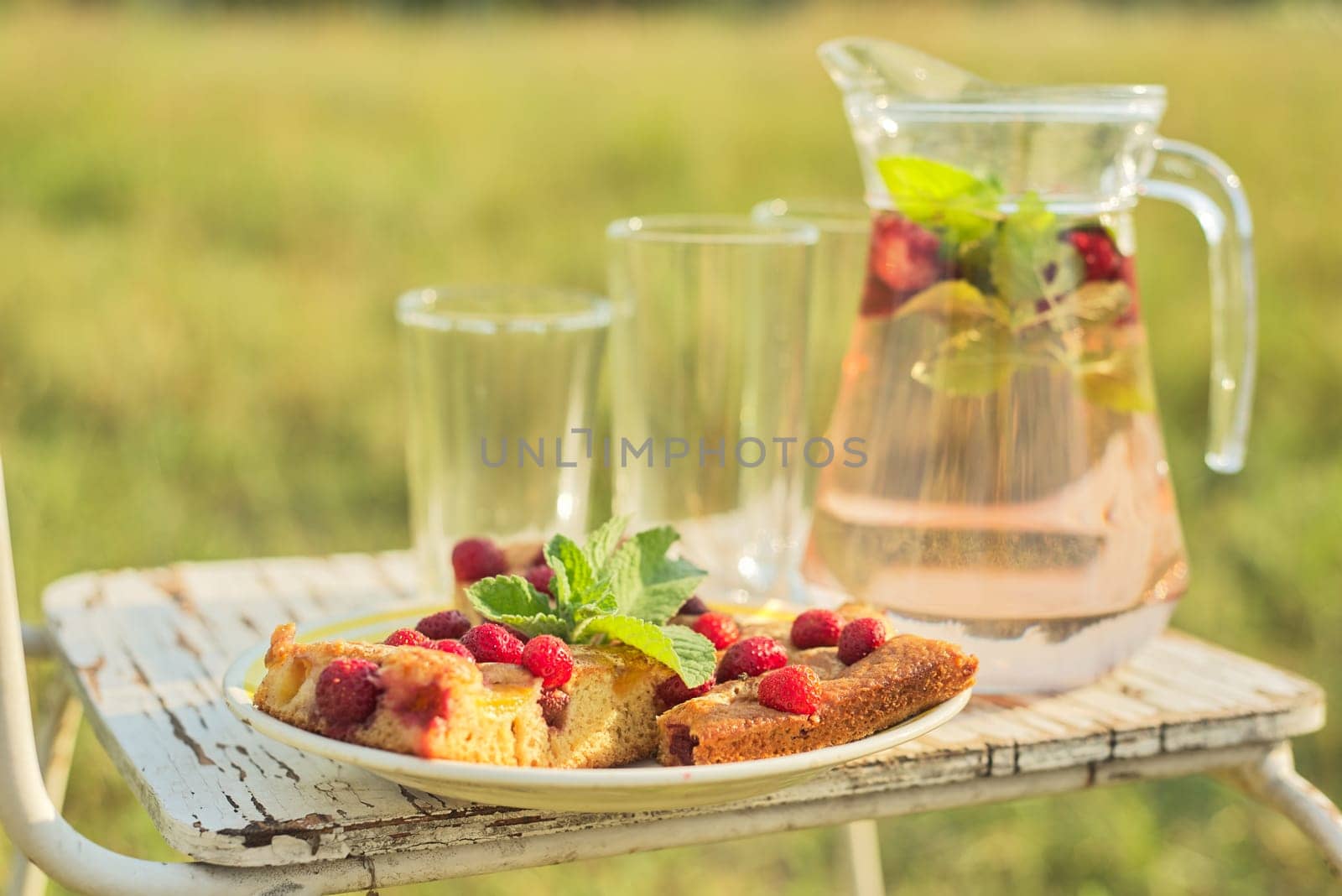 Cake with berries and jug with strawberry mint drink in summer sunny meadow by VH-studio