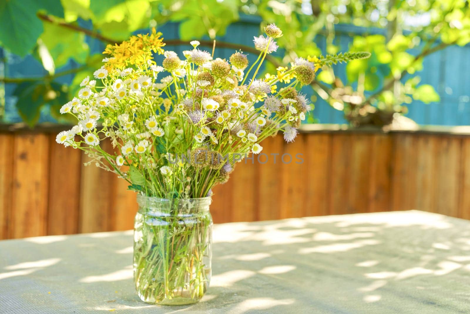 Bouquet of summer wildflowers and herbs in jar on table on terrace, sunny day, rustic style