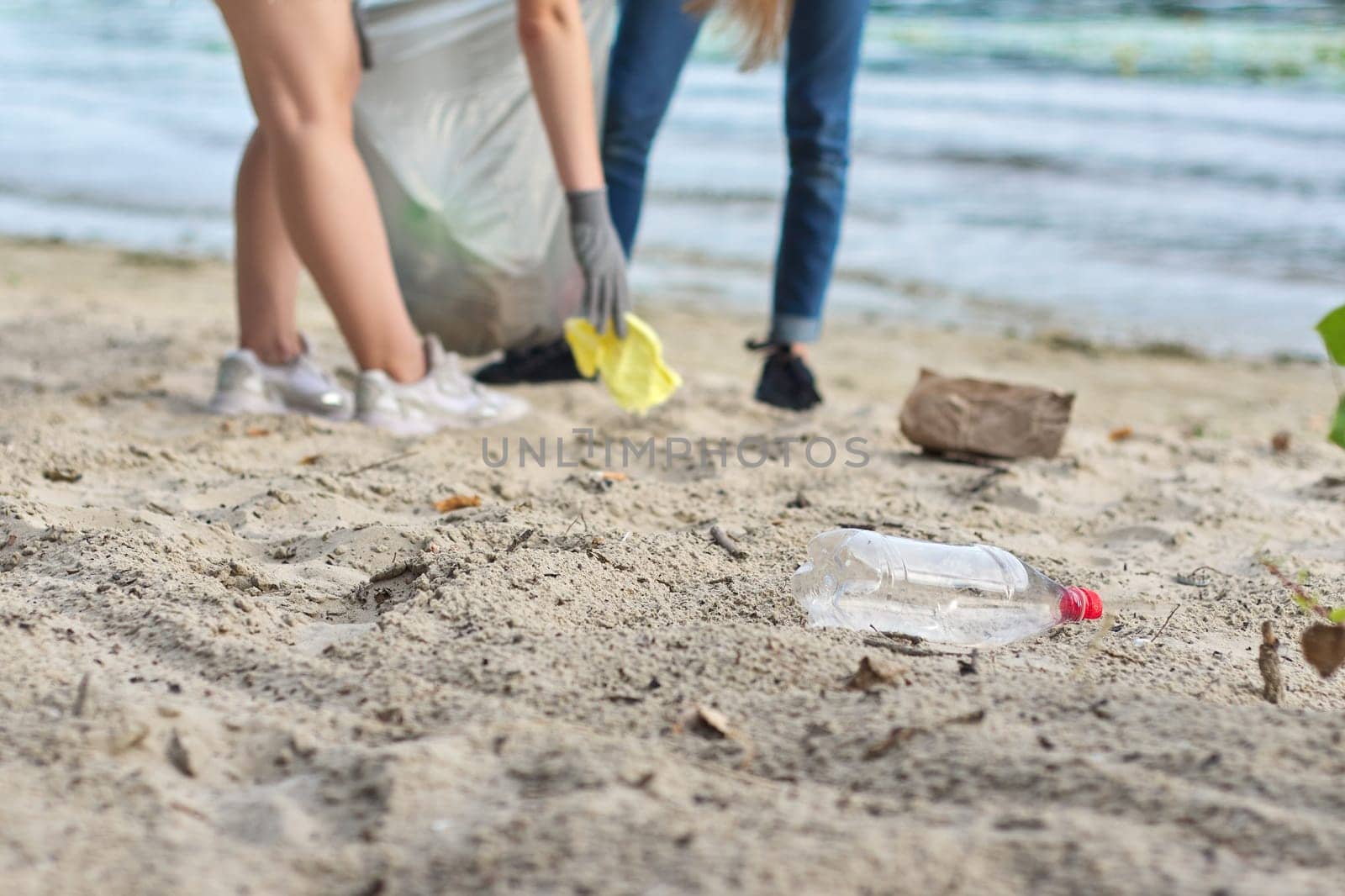 Group of teenagers on riverbank picking up plastic trash in bags by VH-studio