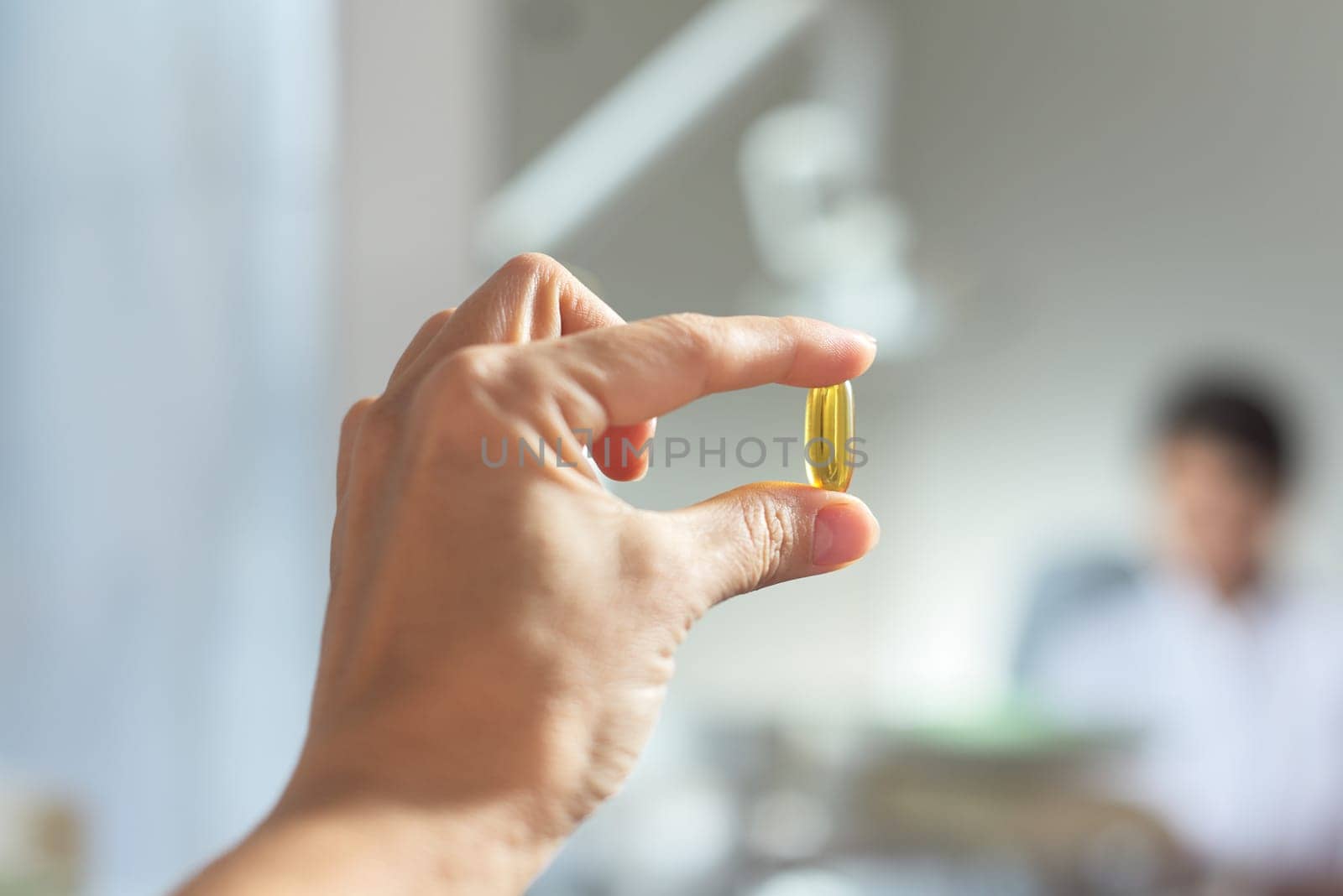 Yellow gel capsule of vitamin D, E, omega-3 in womans hand close-up by VH-studio