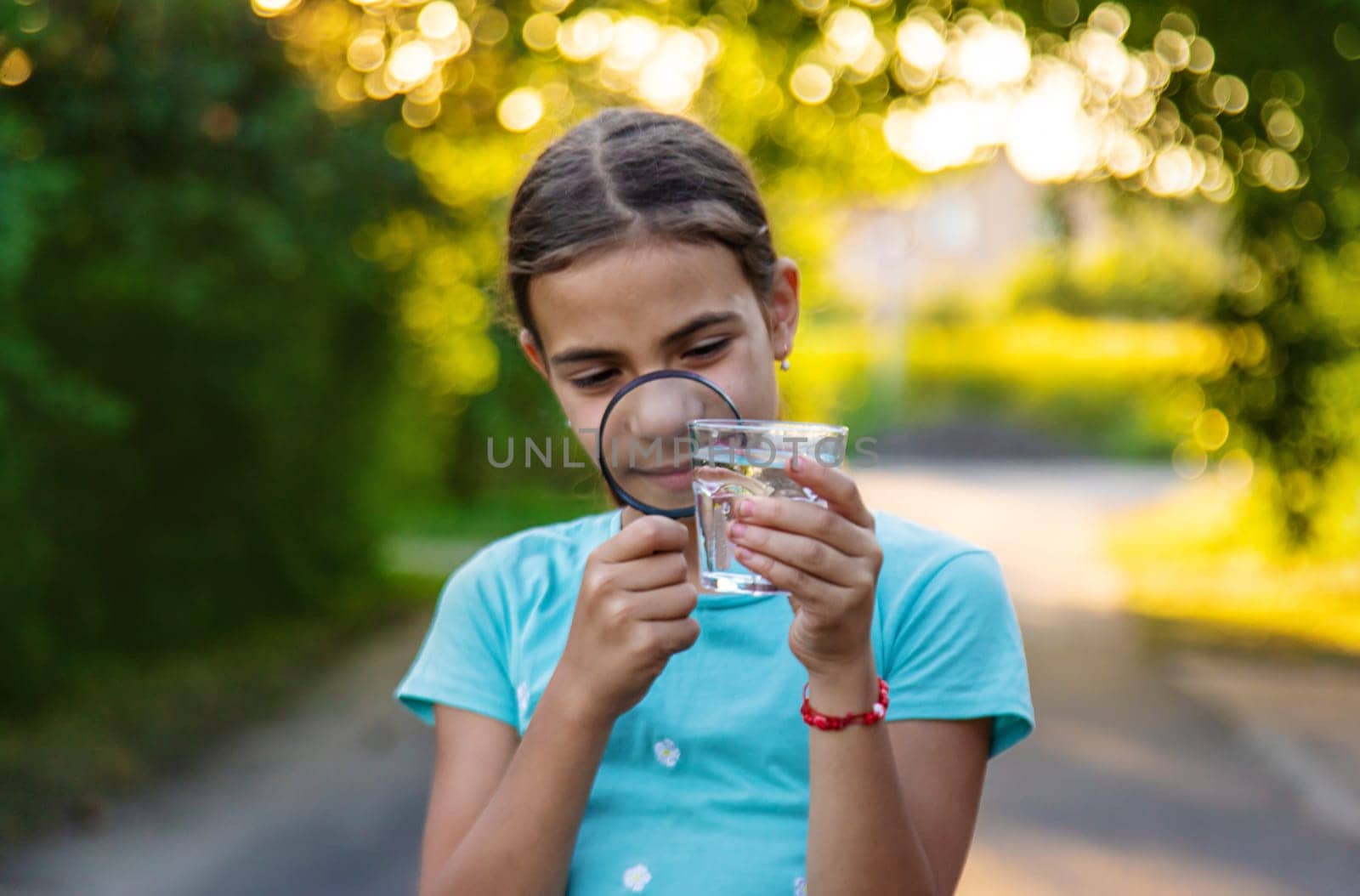 A child looks into a glass of water with a magnifying glass. Selective focus. Drink.