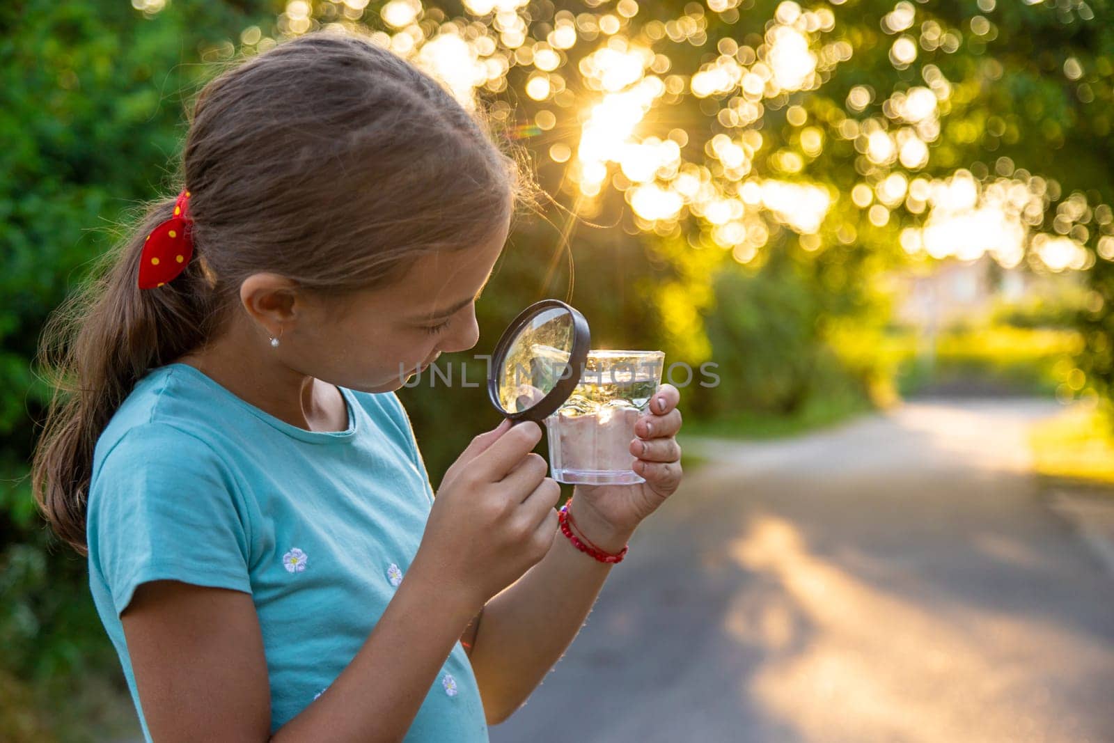 A child looks into a glass of water with a magnifying glass. Selective focus. Drink.