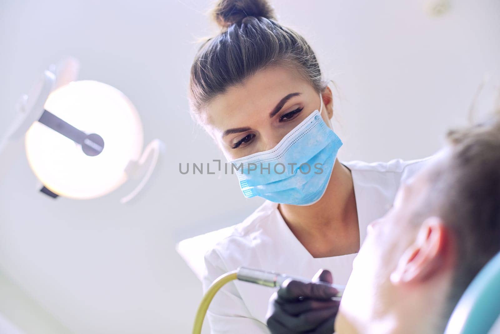 Female dentist treating teeth to patient, young man in chair at dental clinic. Dentistry, healthy teeth, medicine and healthcare concept