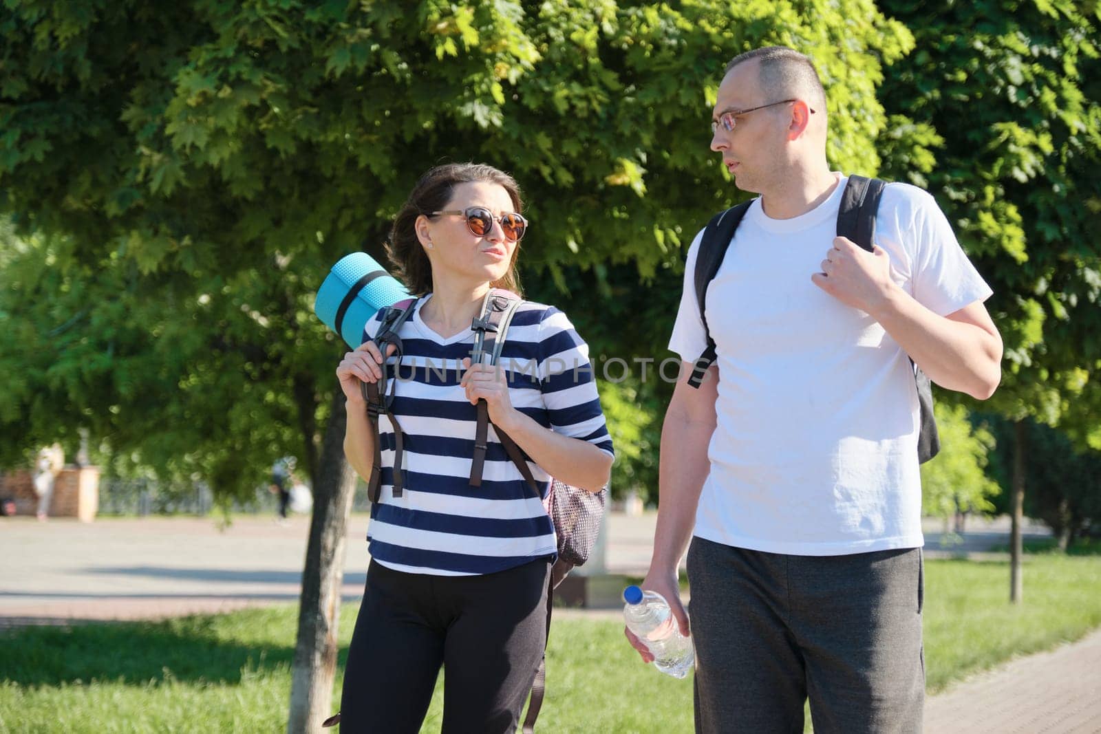 Talking middle-aged man and woman, couple walking along park road for sports fitness training, active healthy lifestyle and relationships of age 40 years old people