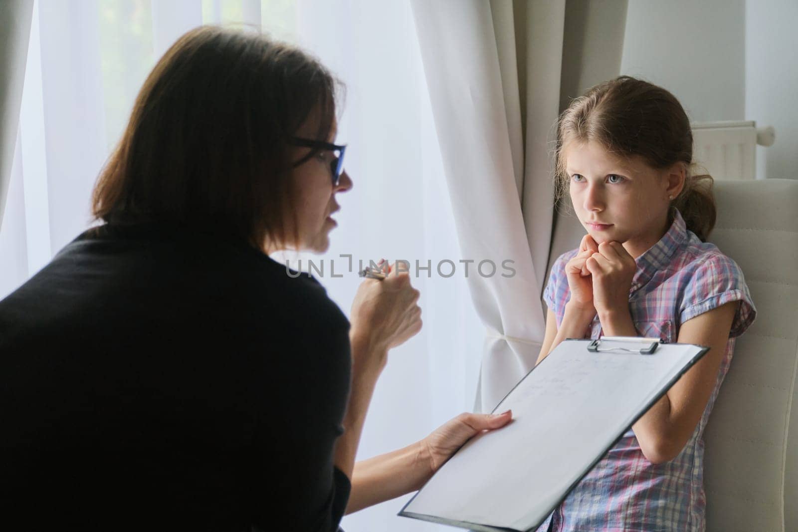 Meeting child girl with school counselor therapist. Children mental health, psychological assistance, counselor takes notes on clipboard