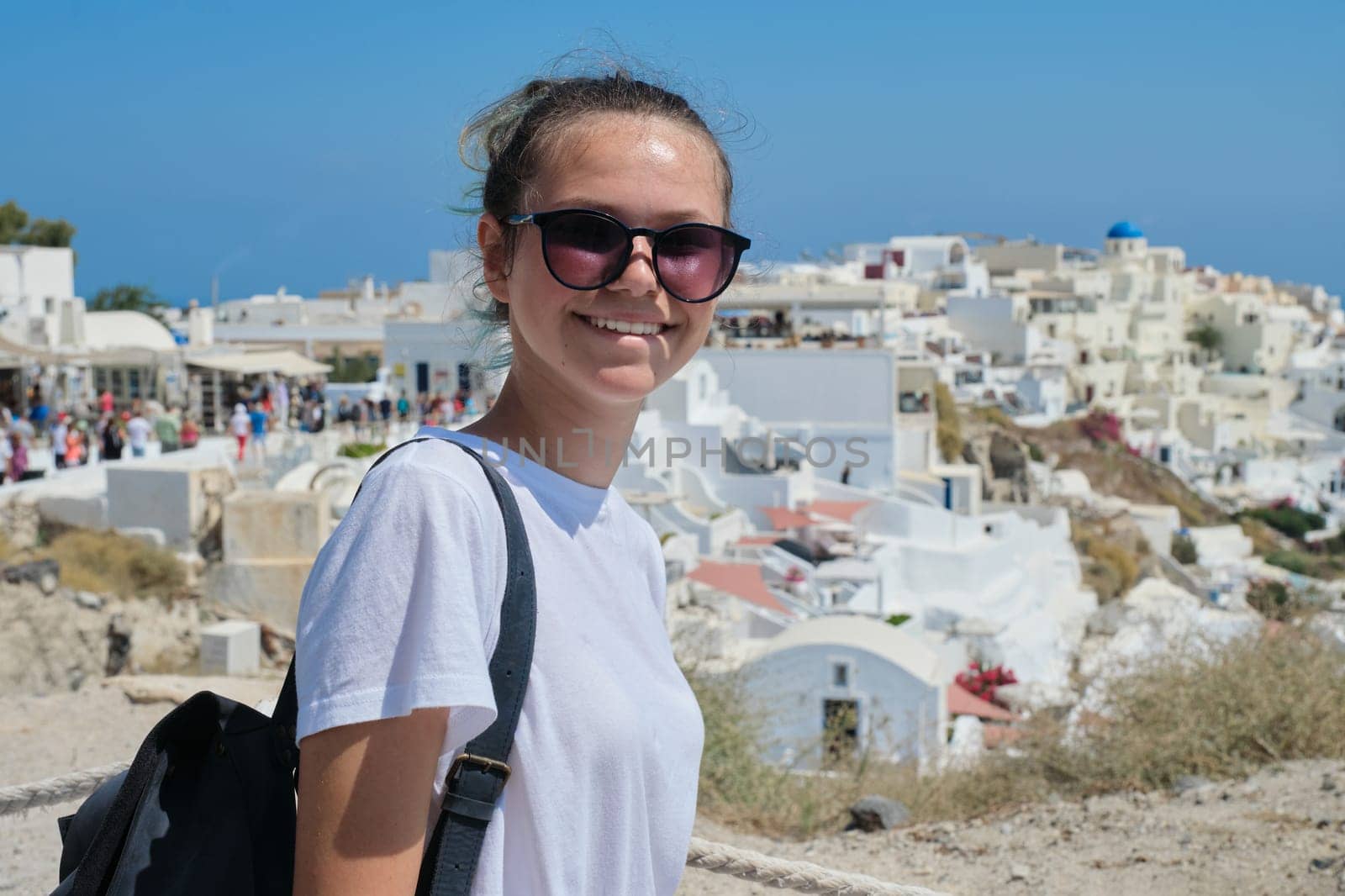 Young beautiful girl tourist visiting Greek islands, smiling teenager posing on the island Santorini, from Oia, Greece. Europe travel cruise vacation destination