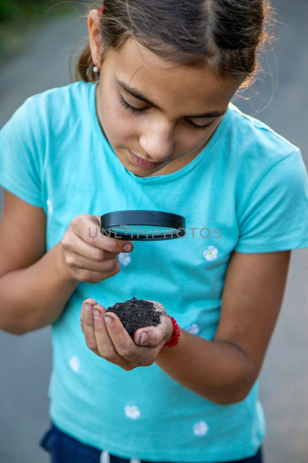 The child looks at the soil in his hands with a magnifying glass. Selective focus. Kid,