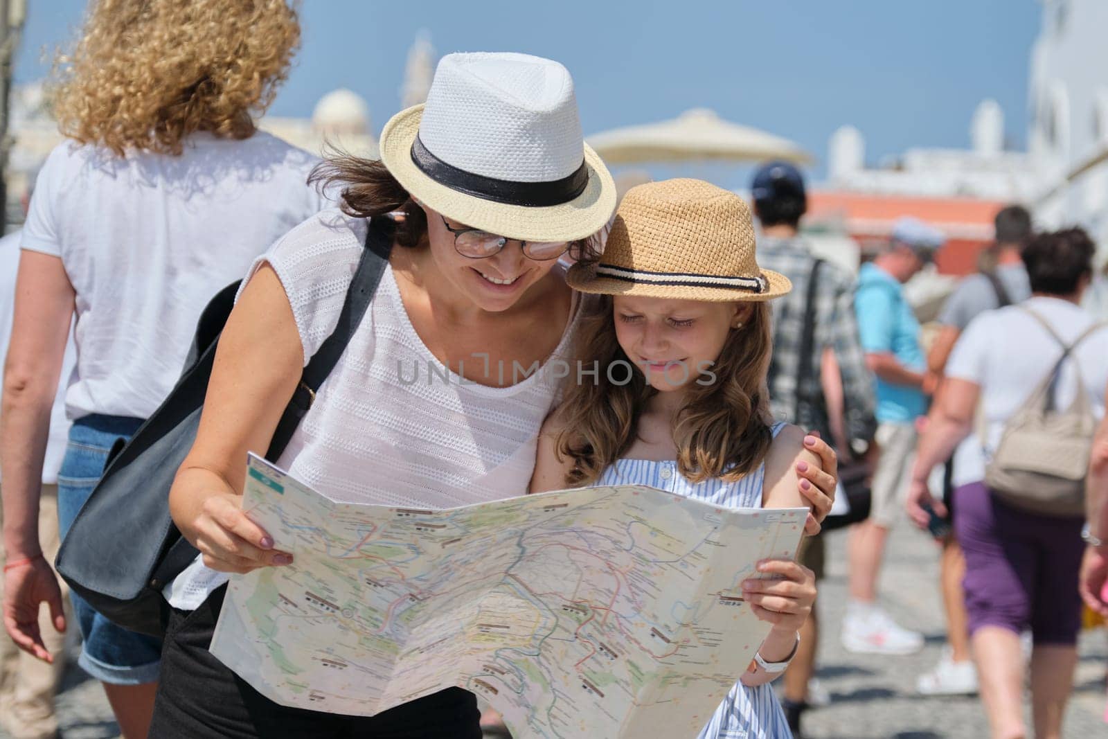 Summer vacation together, family mother and little child daughter traveling, reading map, background walking people tourists, sunny day
