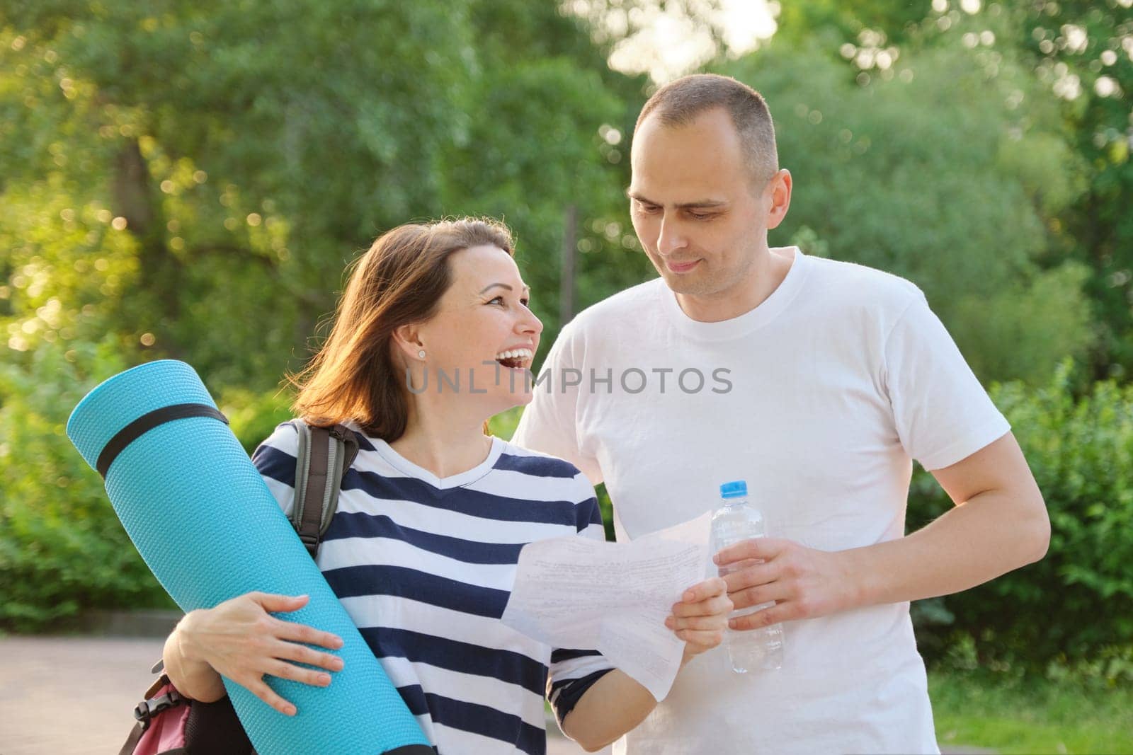 Mature active couple outdoor for healthy lifestyle, smiling woman and man reading paper letter, emotion of joy happiness