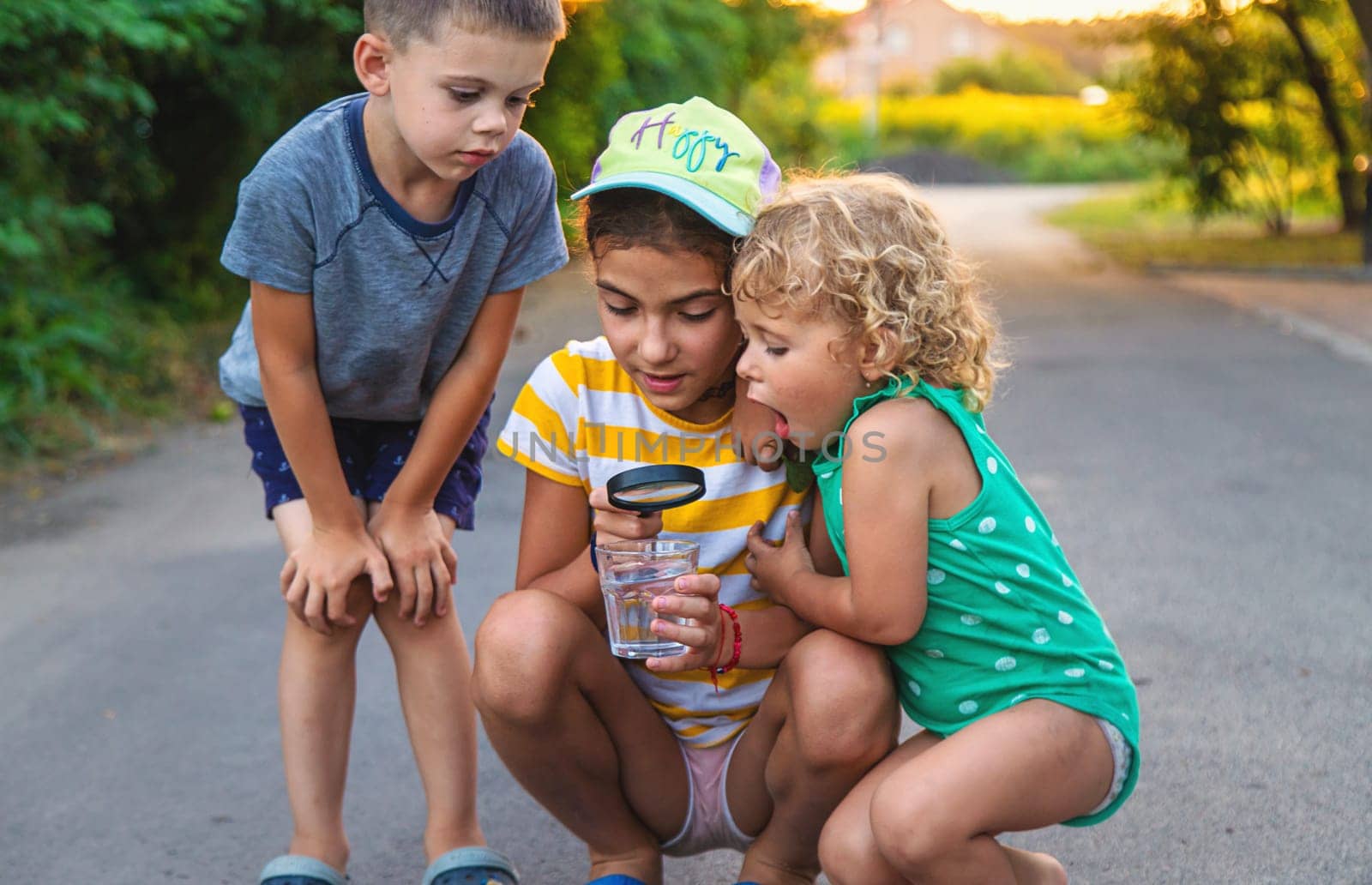 Children look with a magnifying glass into a glass of water. Selective focus. by yanadjana