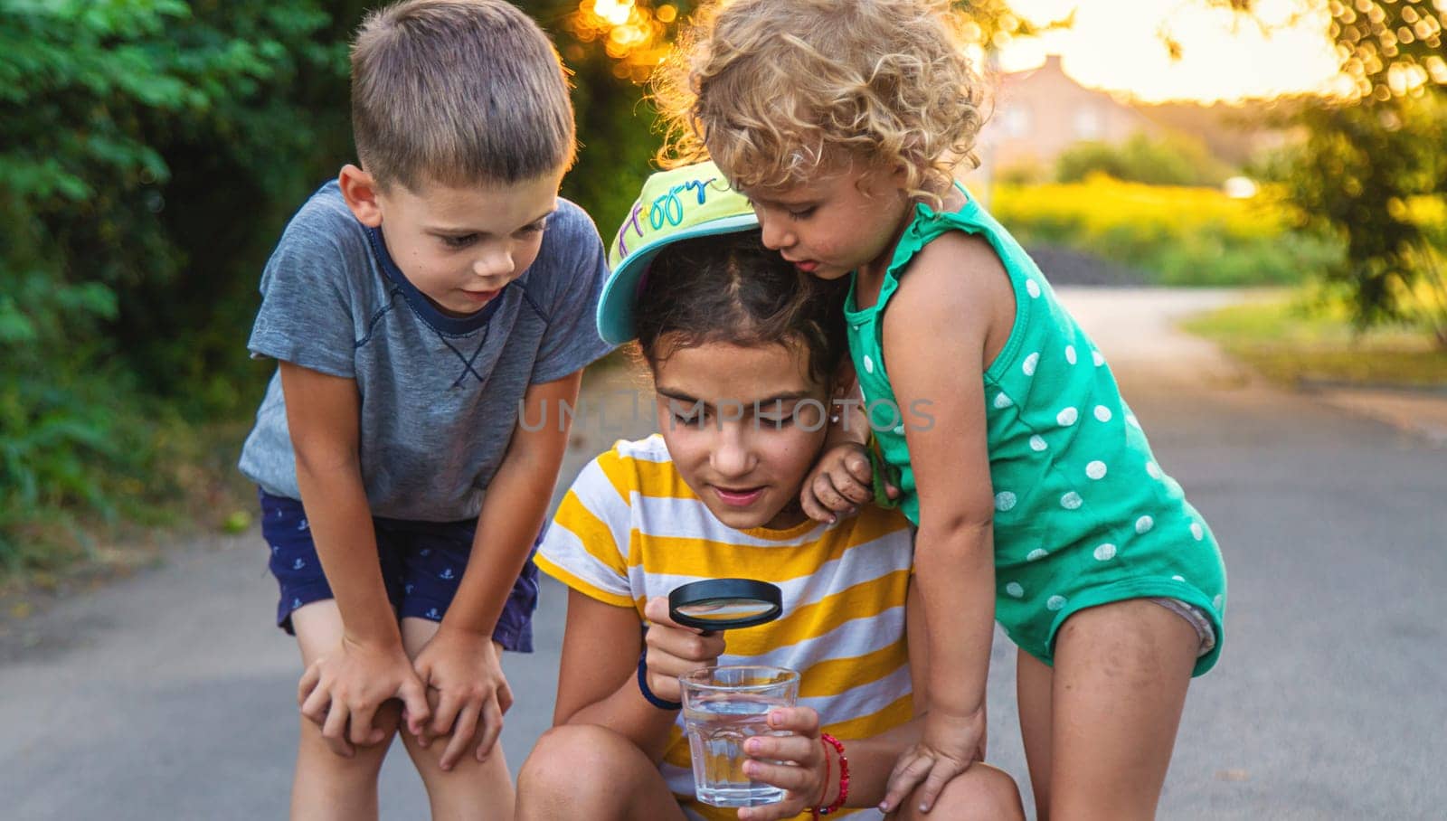 Children look with a magnifying glass into a glass of water. Selective focus. Kid.