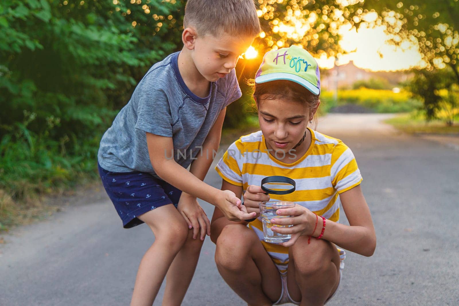 Children look with a magnifying glass into a glass of water. Selective focus. Kid.